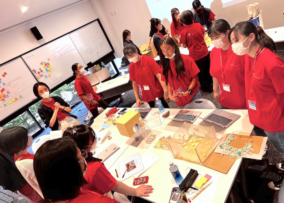 Design coaches guide the youths at the workshop. At OIST, a doctoral student engages and collaborates with them using the human-centered approach. 
